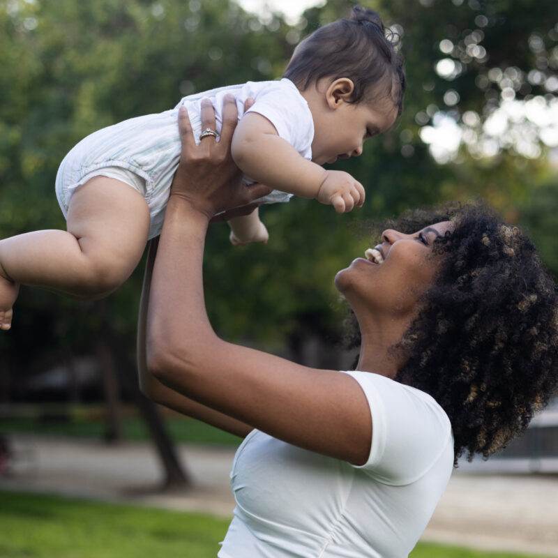 A mom holding her baby in the air and smiling
